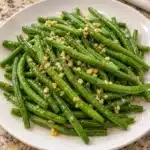 Tender-crisp green beans coated in lemon garlic butter on a white serving plate